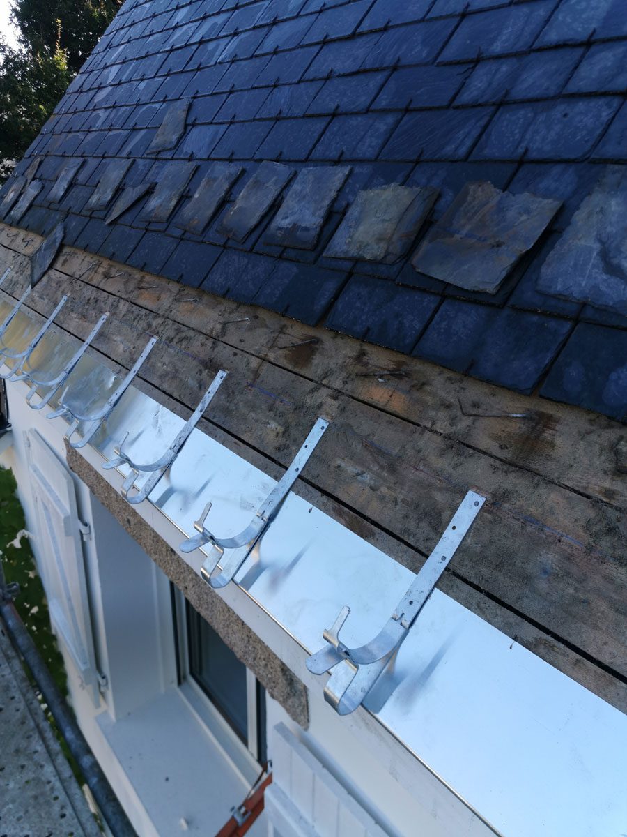 Bas de pente d'une toiture en ardoise en rénovation à Vannes : bande d'égout en zinc et crochets de gouttière posés avant la repose des ardoises