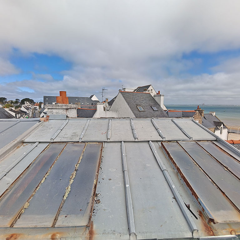 Toit en zinc usé, avec des plaques rouillées et des joints dégradés, face à la mer à Saint-Malo